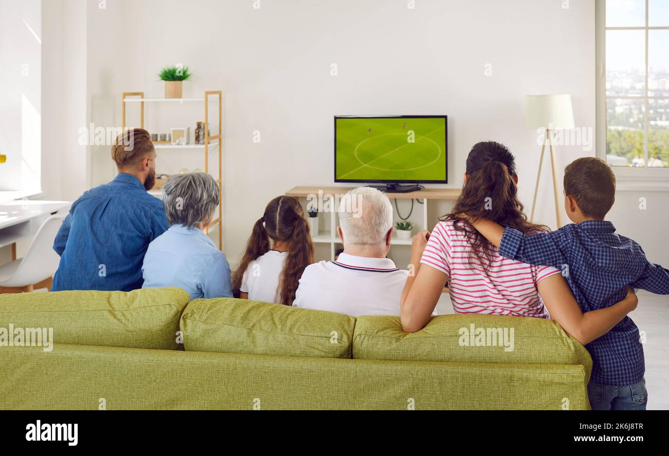 Multi-generational family is watching football match on TV together at home sitting on sofa. Stock Photo