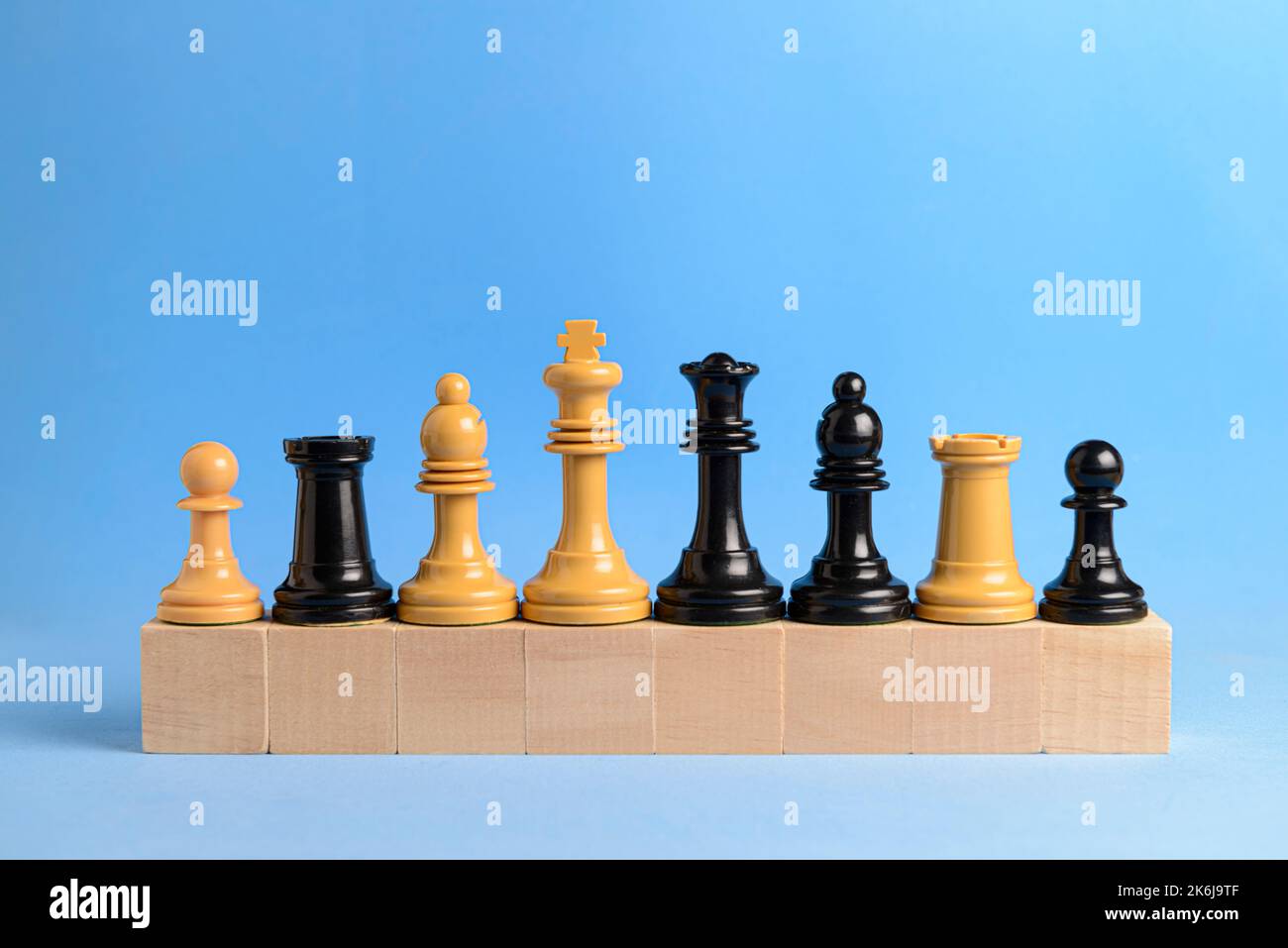 White and black chess pieces on wooden blocks with blue background. Concept of teamwork and cooperation. Stock Photo
