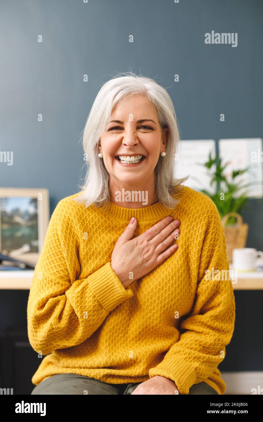 Vertical image of happy caucasian senior woman making video call smiling to camera, touching chest Stock Photo