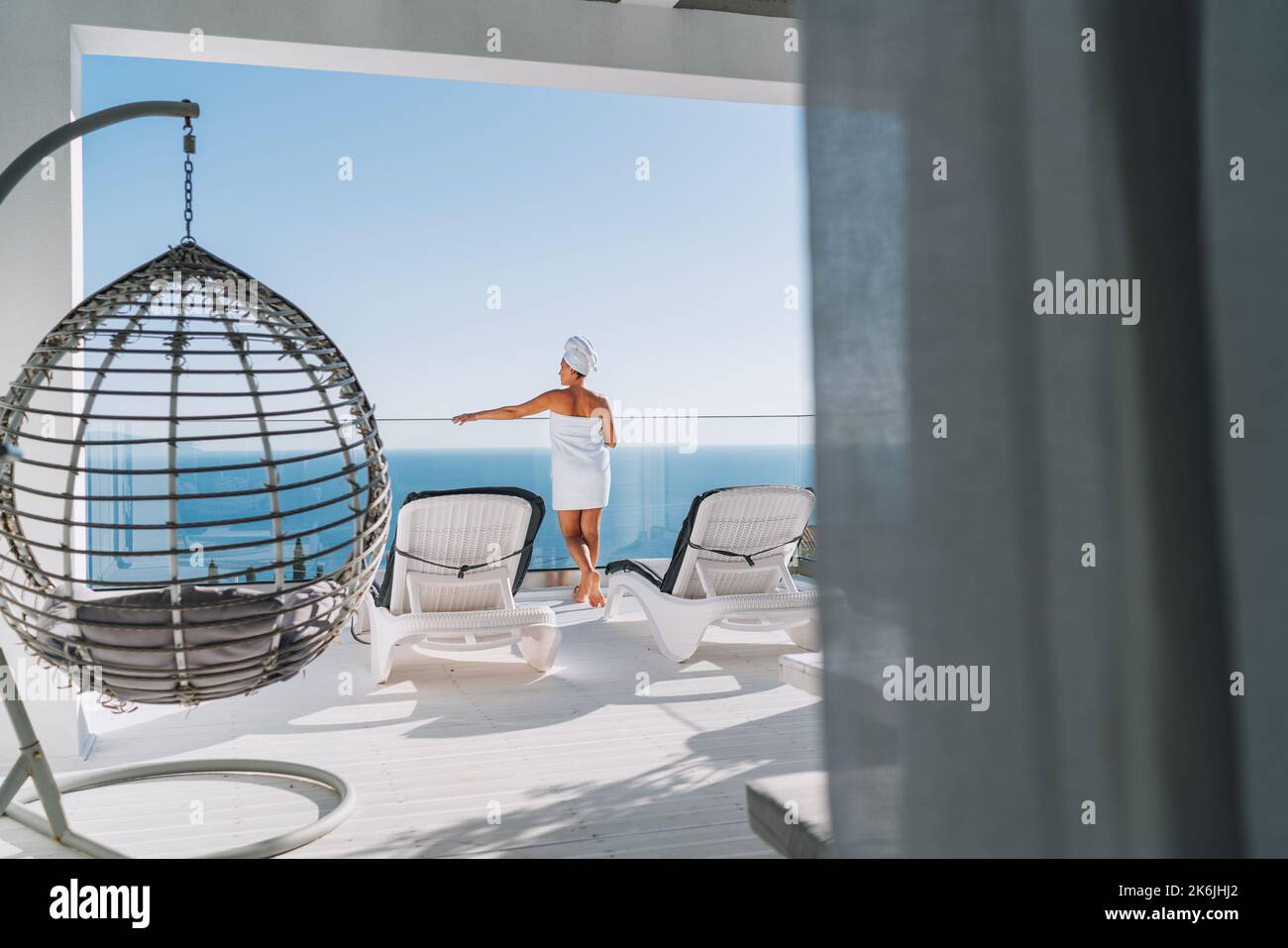 After shower beautiful woman with hair and body towel wrap standing on open house terrace with