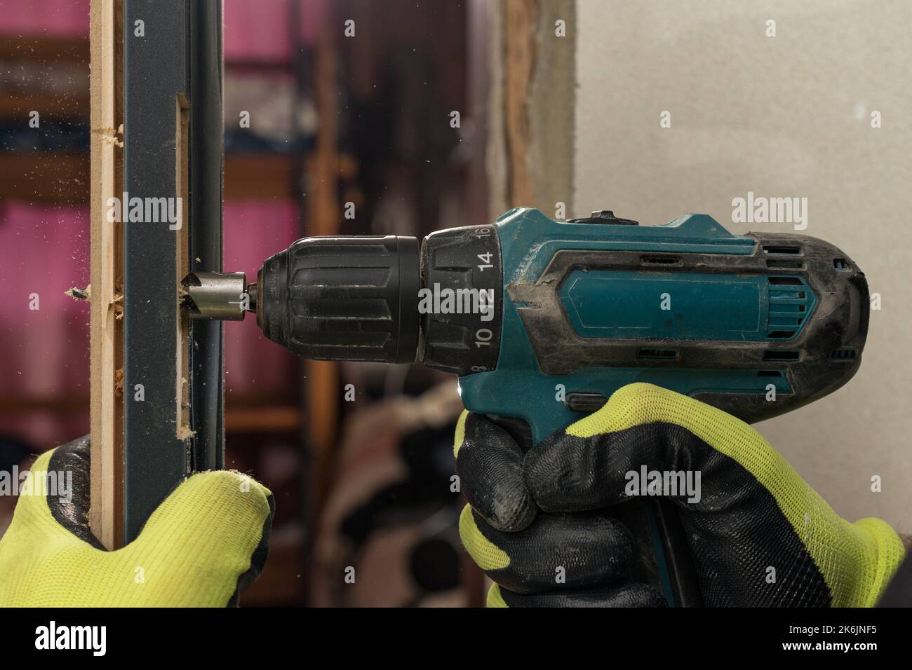 Drilling a hole in the door with a green screwdriver, closeup of the