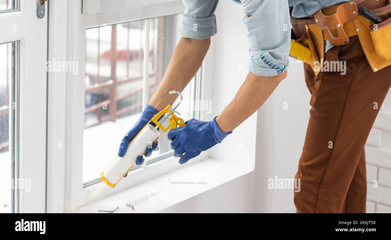 Construction worker sealing window with caulk indoors Stock Photo