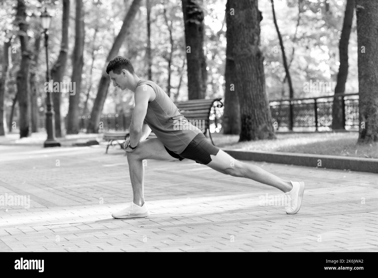 Sportsman hold lunge position doing stretch routine during outdoor athletic workout in park, warmup Stock Photo