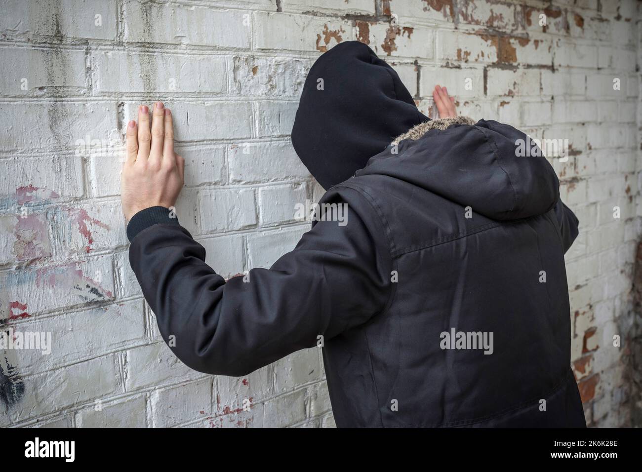 Addict alone in an abandoned building, against a white brick wall. Side