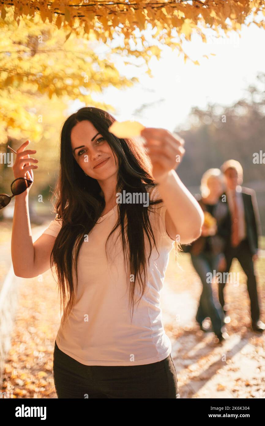 Happy smiling young woman holding yellow leaf in front of her face ...