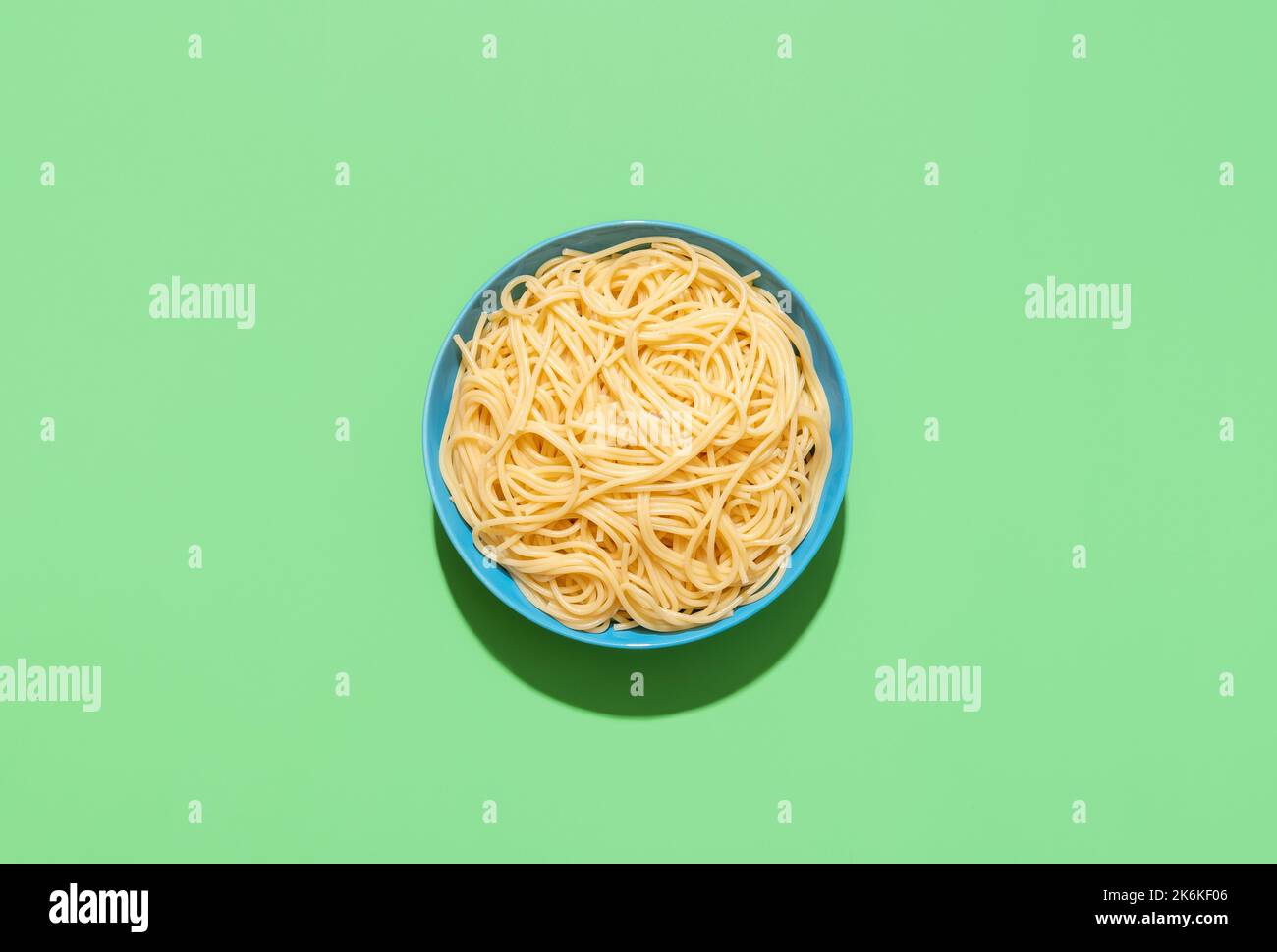 Above view with a blue plate with spaghetti minimalist on a green table. Spaghetti without sauce in bright light on a colorful background Stock Photo