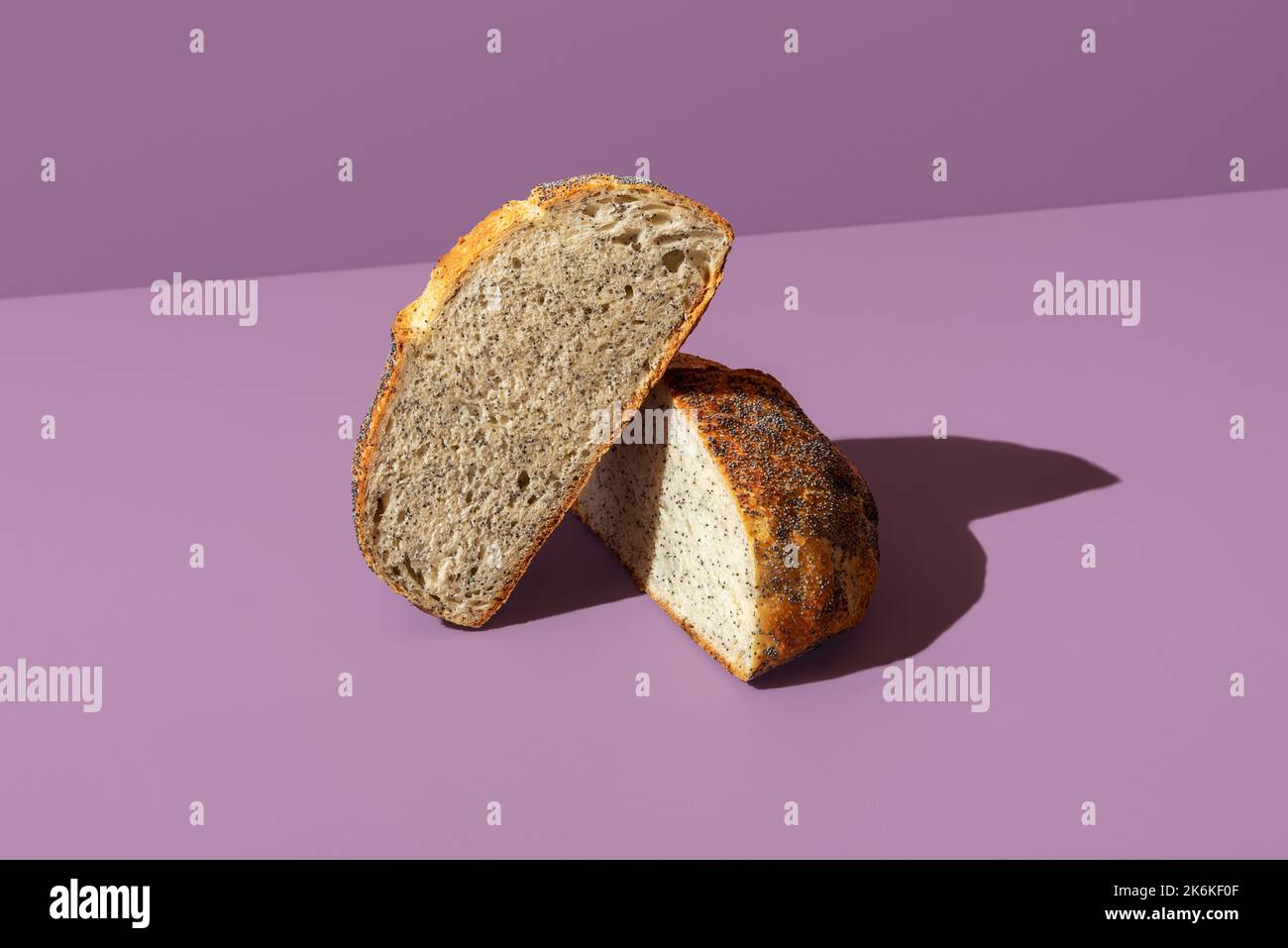 Delicious homemade bread with poppy seeds minimalist on a purple-colored table. Loaf of bread sliced in two halves. Stock Photo
