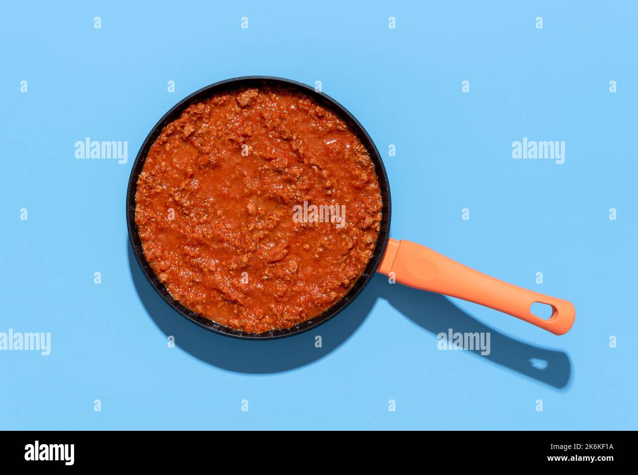 Above view with a pan with bolognese sauce isolated on a blue background. Classic italian sauce with minced meat and tomato sauce Stock Photo