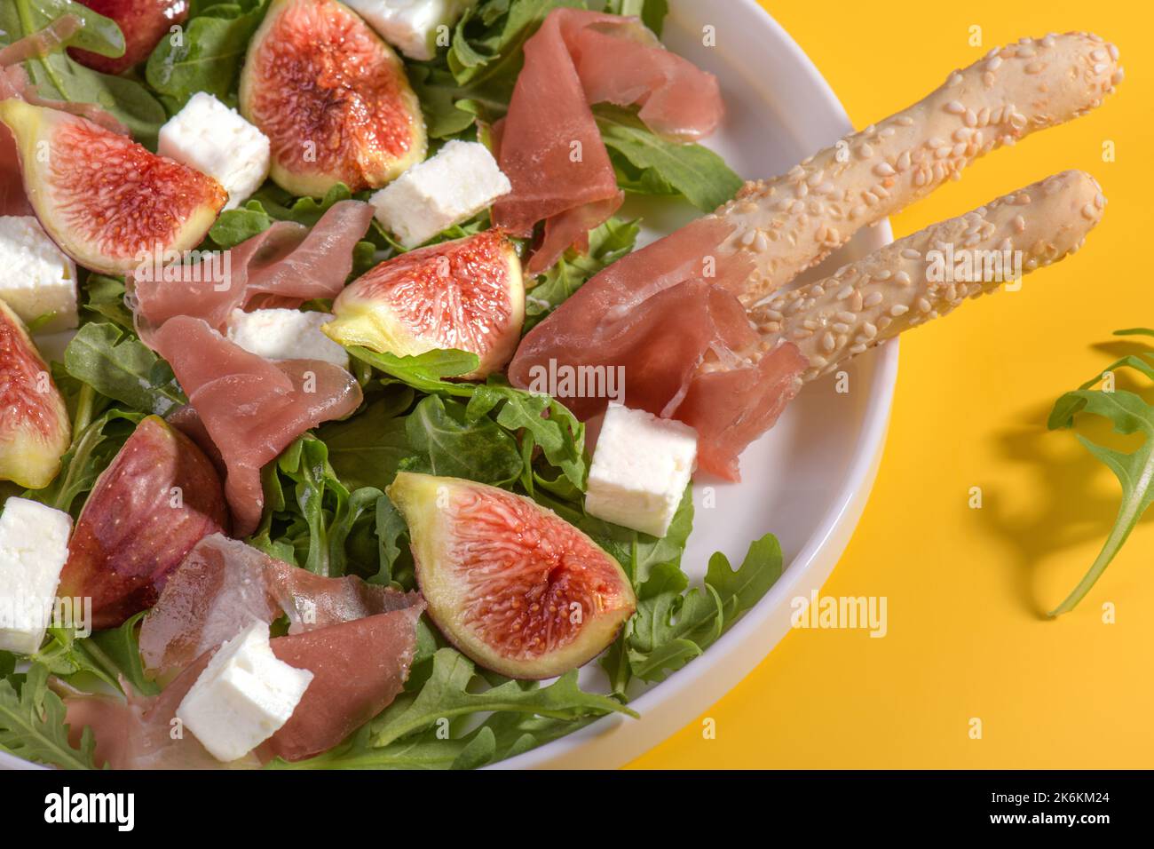 Autumn figs salad with arugula, feta, raw ham in white plate on yellow