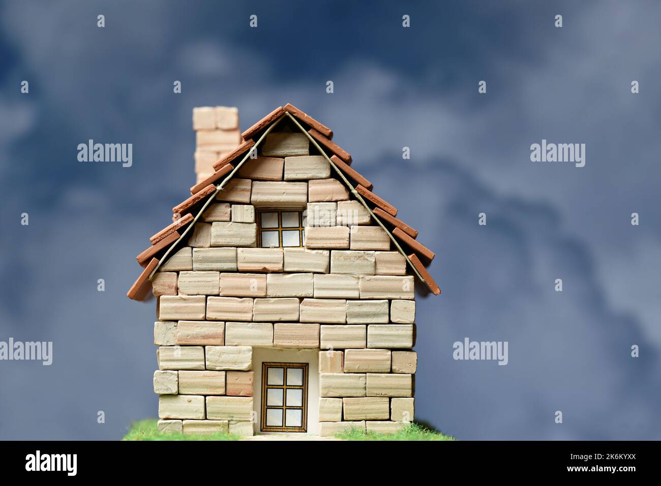 Casita hecha de ladrillos de piedra en miniatura con nubes de fondo Stock Photo