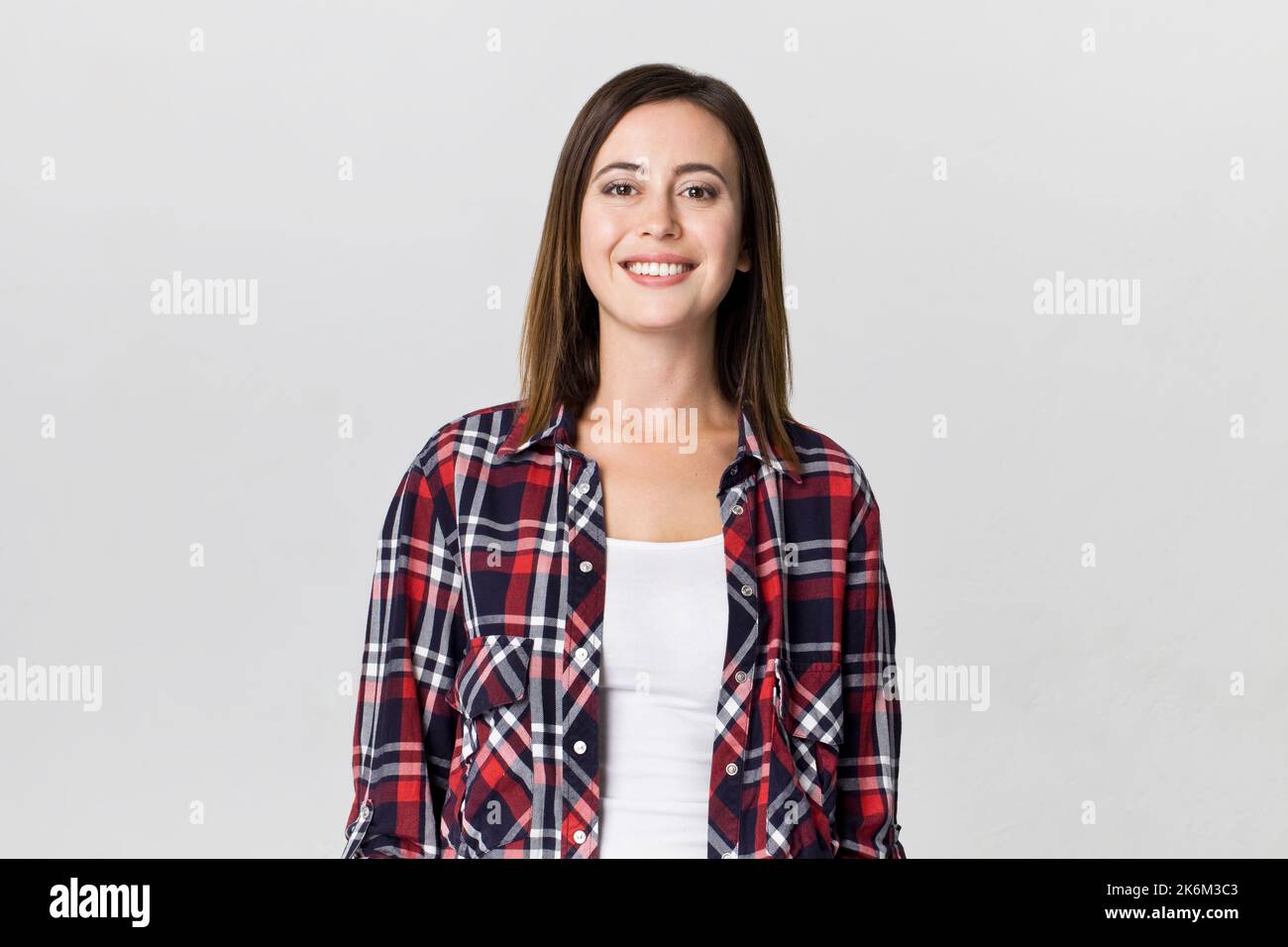 Smiling positive female with attractive look, wearing checkered shirt, posing against white blank wall Stock Photo