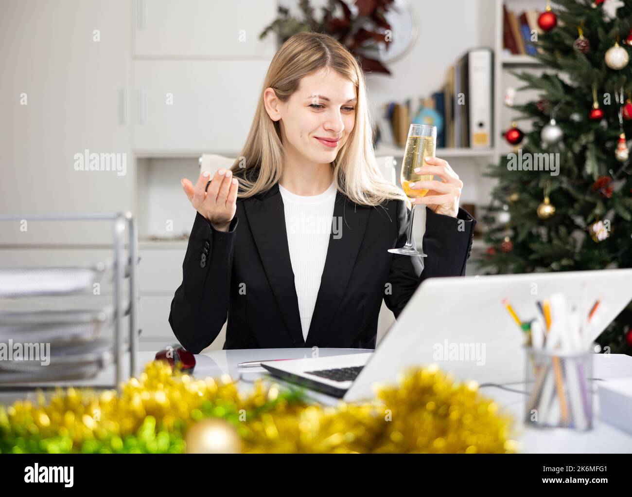 Female manager with a glass of champagne congratulates Merry Christmas on the Internet in office Stock Photo