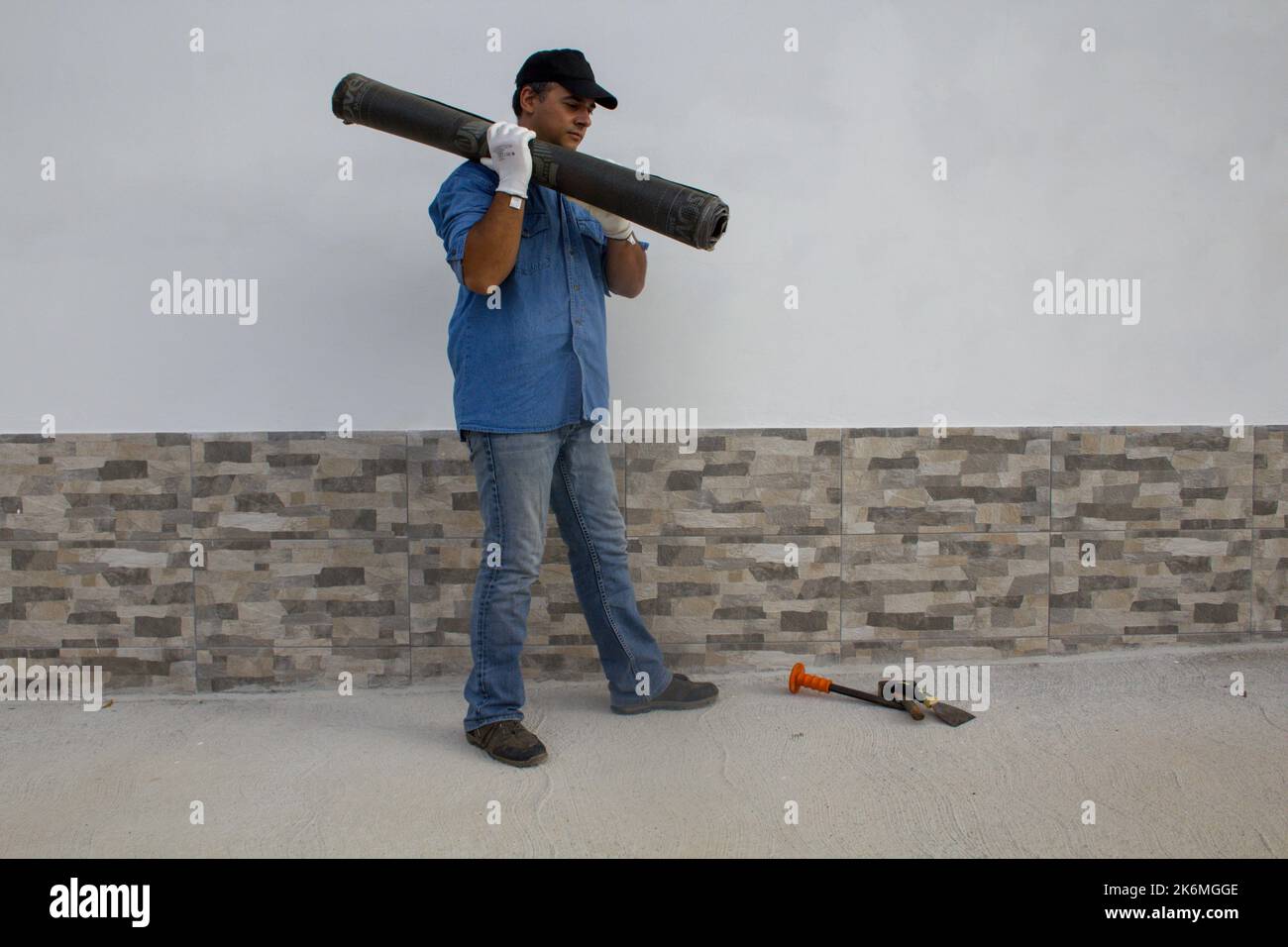 Construction worker carrying a roll of bituminous adhesive sheathing on his shoulder for insulation of roofs and floors. Construction work and protect Stock Photo