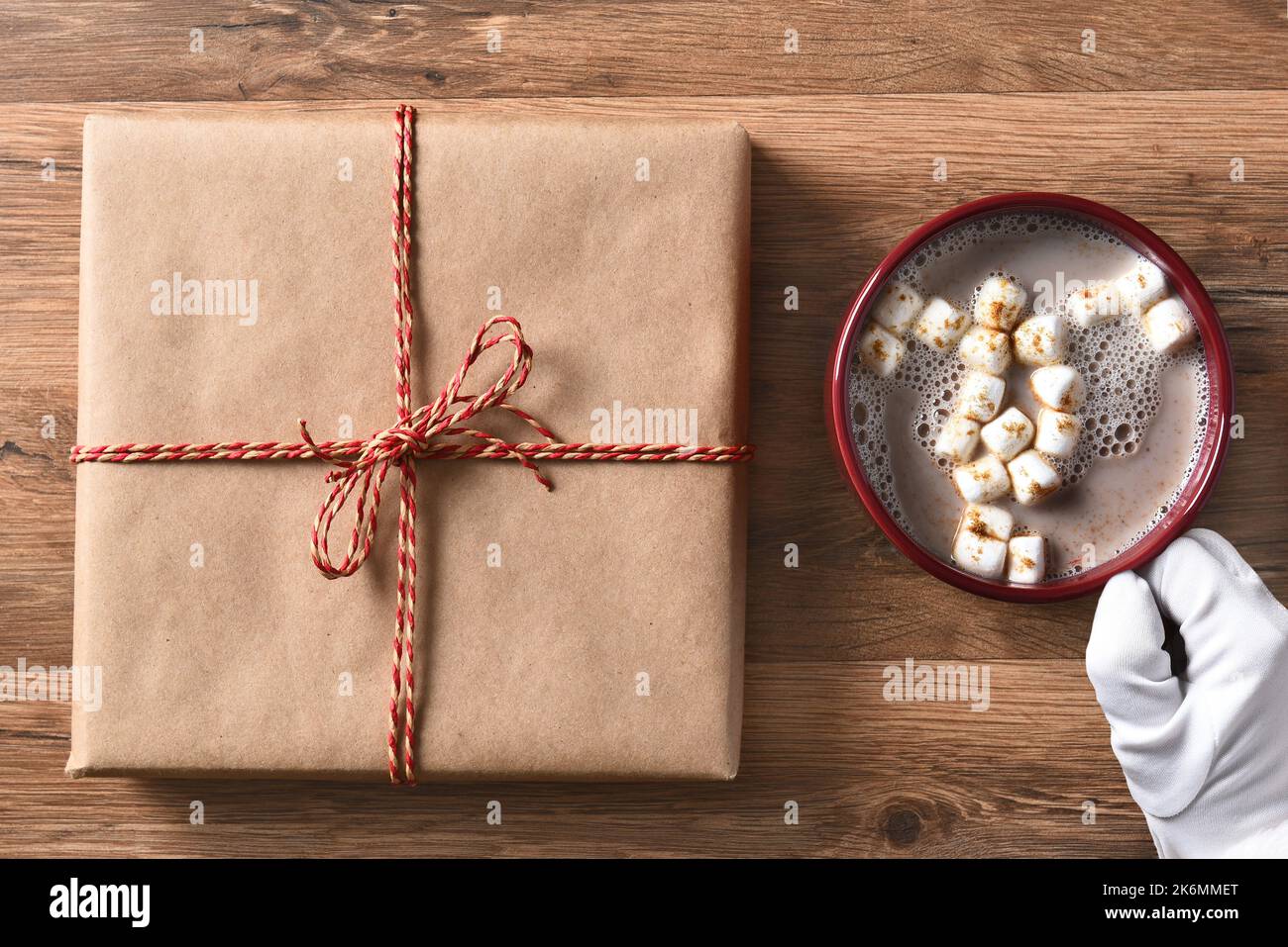 Santa Claus hand with a mug of cocoa and a plain brown paper wapped Christmas present. Stock Photo