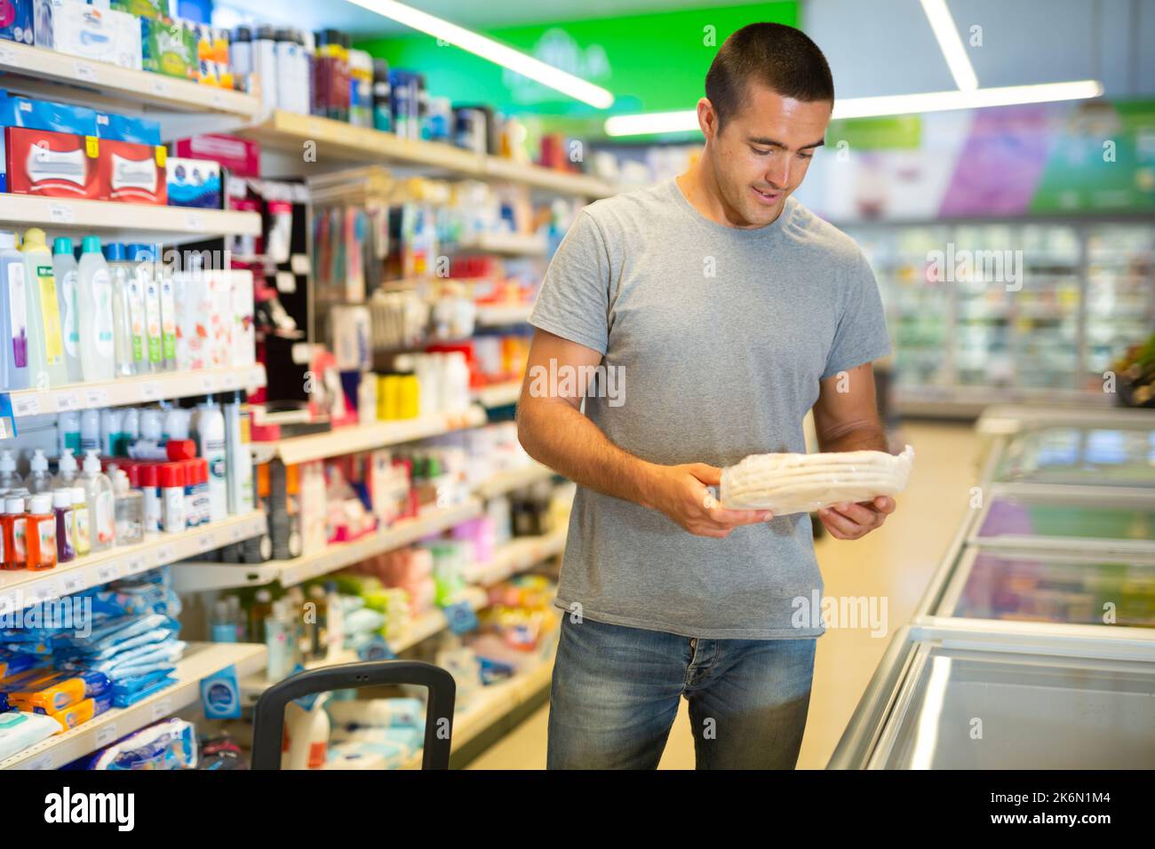 Man choosing frozen pizza dough in refrigerated display case in