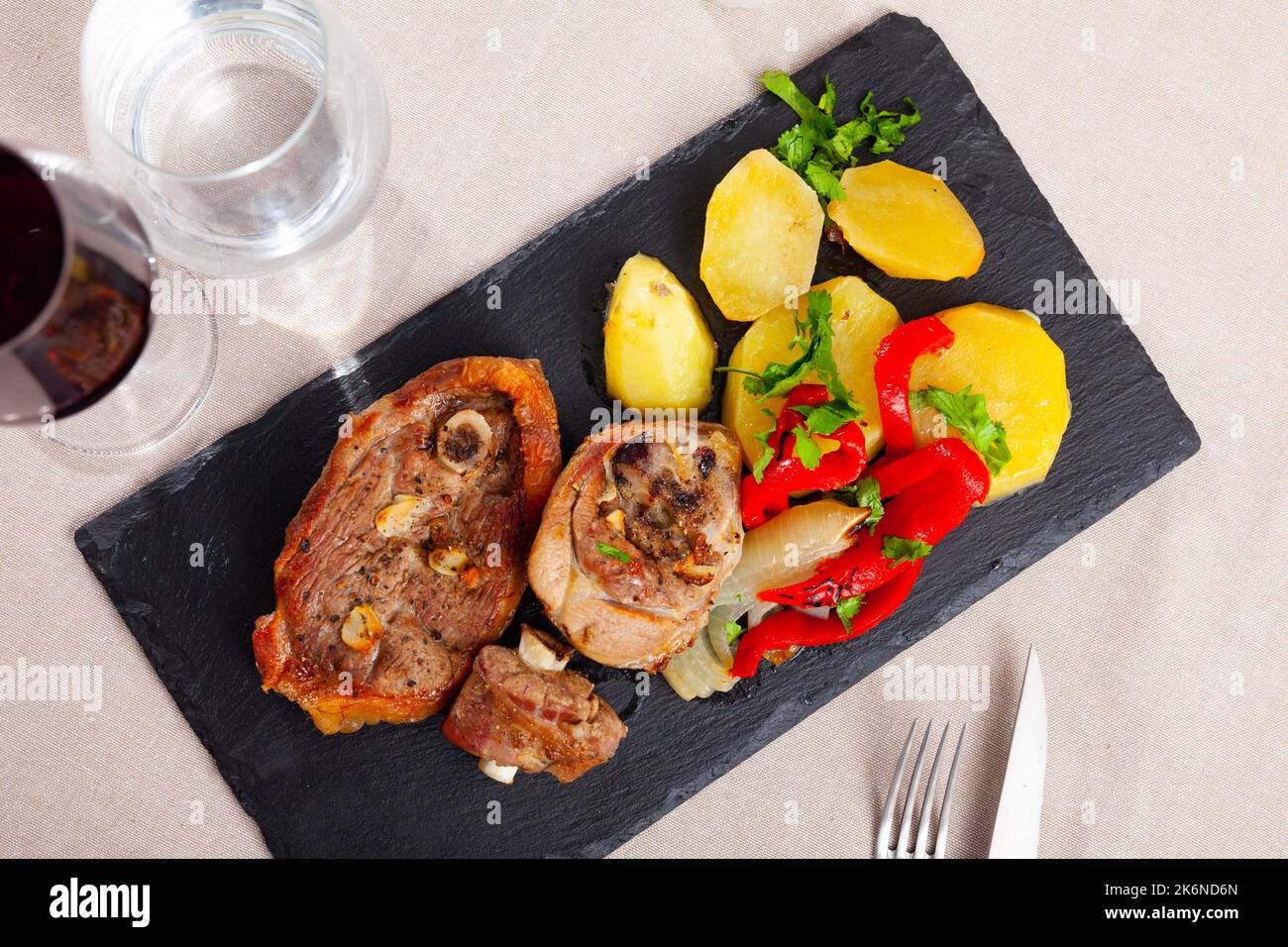Fried lamb leg steaks with potatoes, red pepper slices, greens on slate
