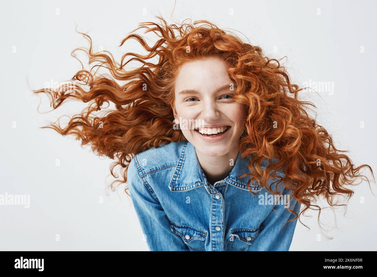 Portrait of beautiful happy cheerful redhead girl with flyingcurly hair smiling laughing looking at camera over white background. Stock Photo