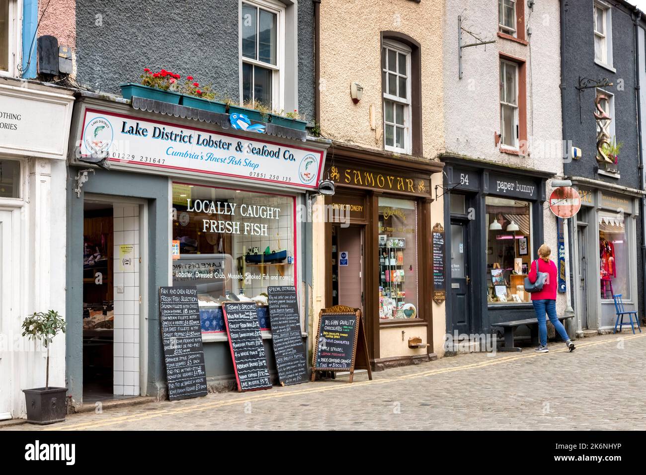 20 May 2022: Ulverston, Cumbria, UK - Independent shops in the high street, with fresh fish shop, confectionary, and others. One woman window shopping Stock Photo