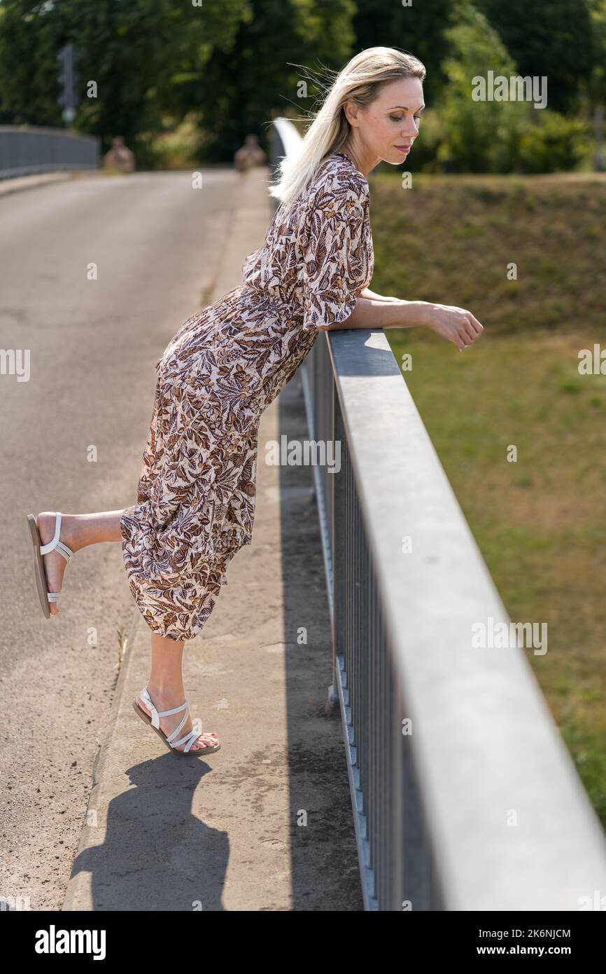 Relaxed Middle Aged Woman Leaning On The Railing Of A Bridge With One relaxed-middle-aged-woman-leaning-on-the-railing-of-a-bridge-with-one