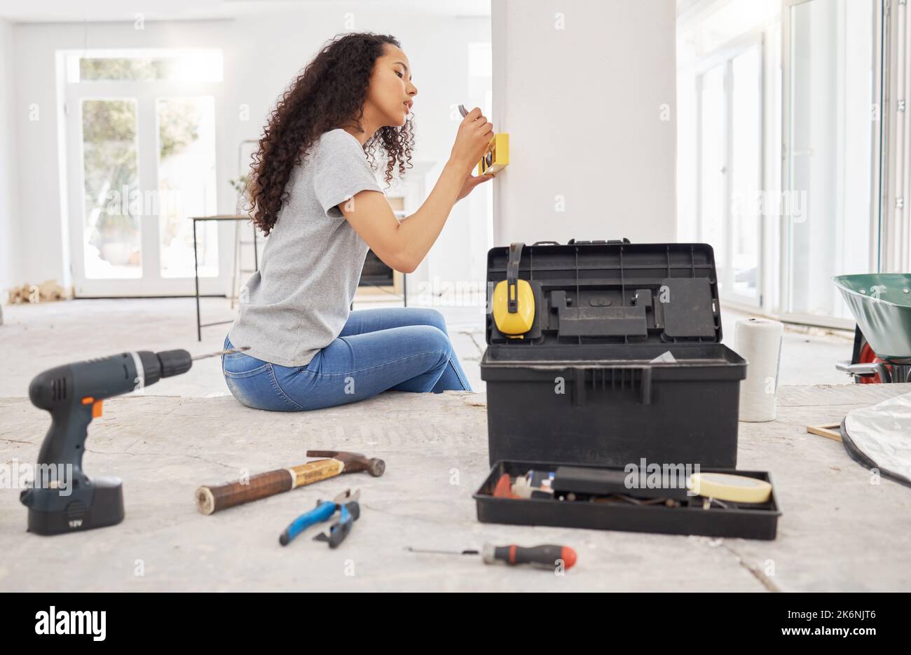 Why wait on others when you can do it yourself. a woman using a spirit level while renovating a house. Stock Photo