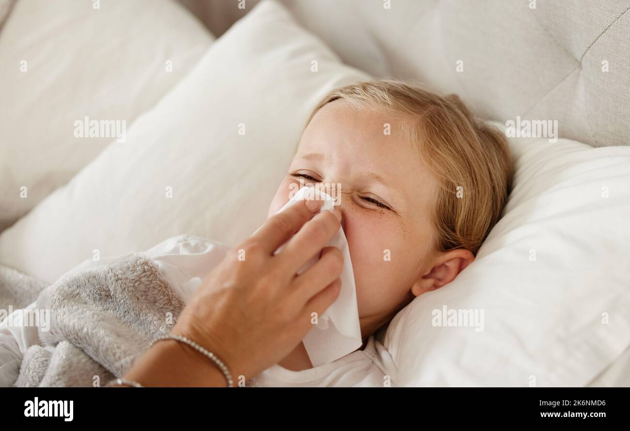 Youll feel better soon. a mother wiping her little girls nose with a tissue in bed at home of a little girl feeling ill in bed at home and blowing her Stock Photo