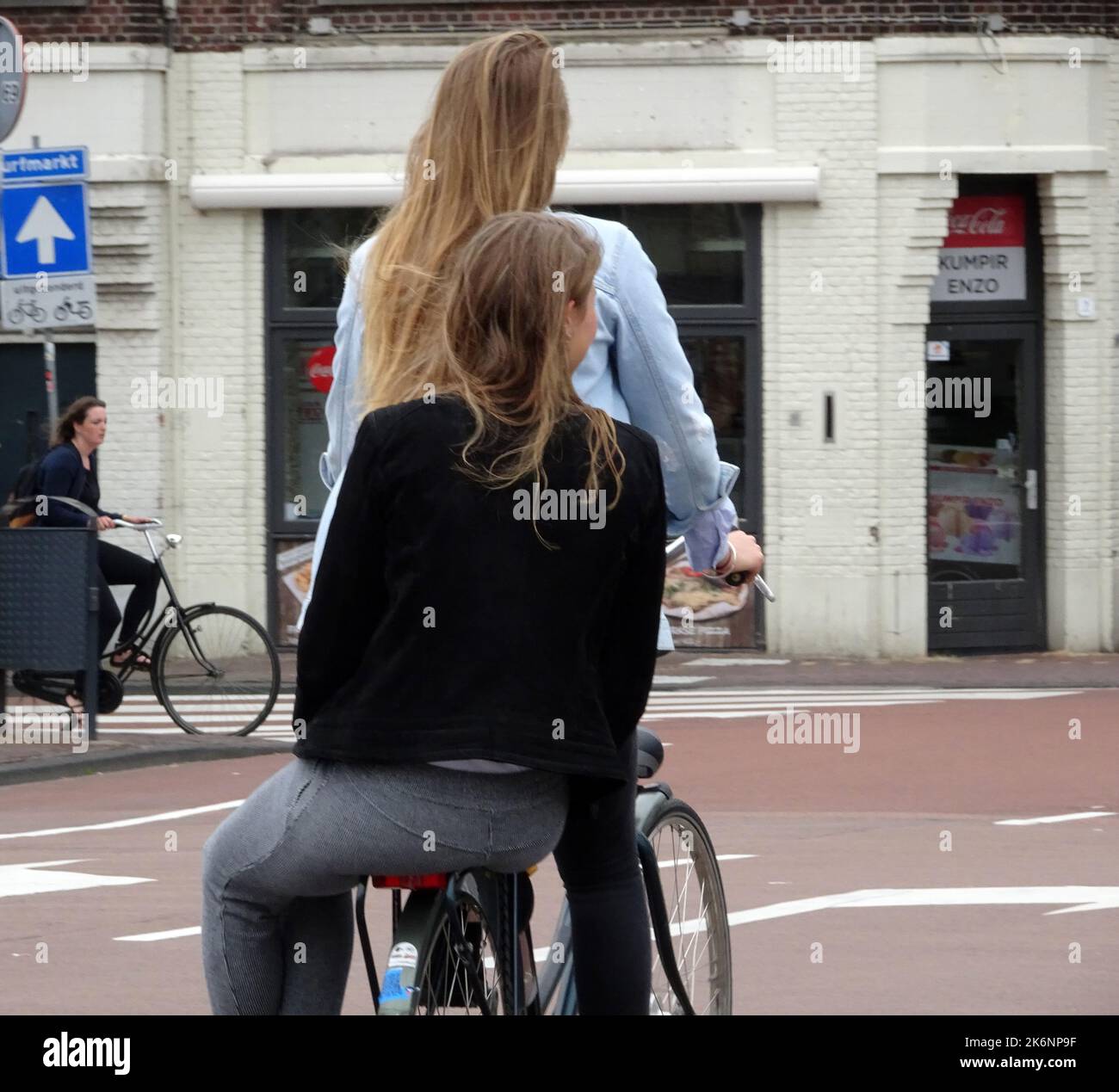 Leiden, the Netherlands - July 8 2016 Two Dutch girls on a bicycle. One is cycling, the other is sitting on the bicycle rack. Stock Photo