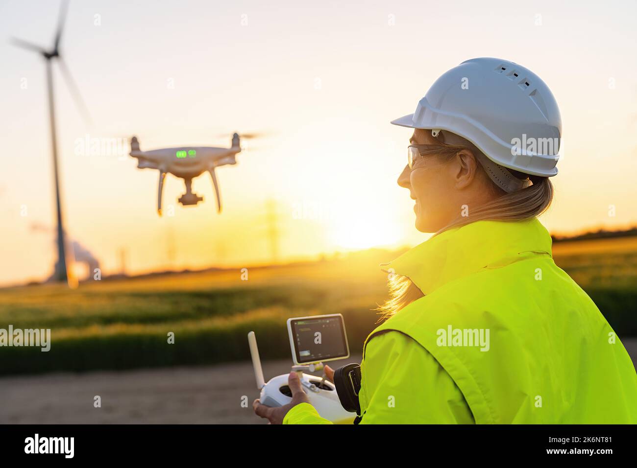 Female Operator inspecting Wind turbine with drone at sunset. Drone
