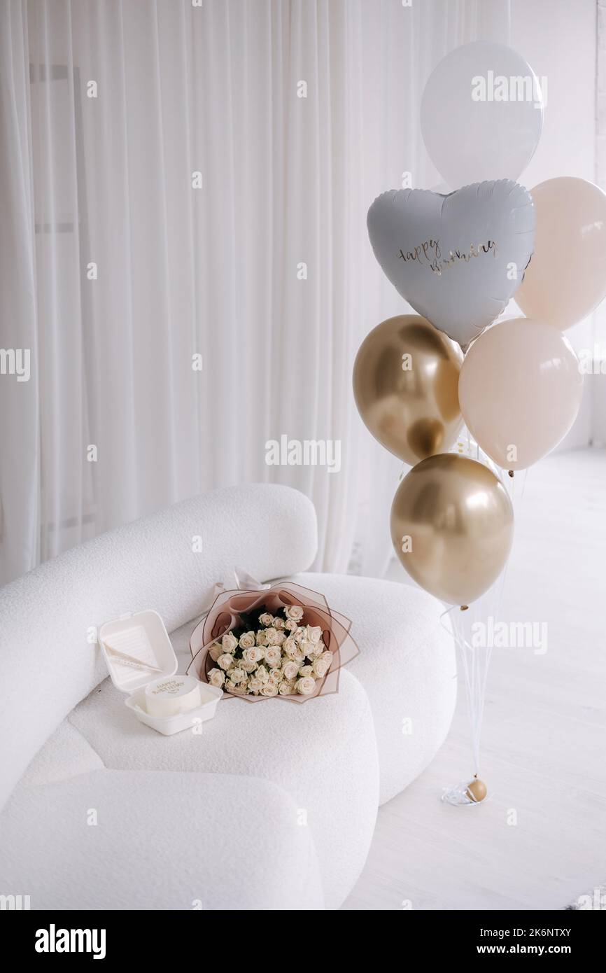 Decorated room at home for surprise party. Bouquet of flowers and banto cake on sofa. Few colorful balloons.Happy birthday for Eighteen-year-old girl Stock Photo