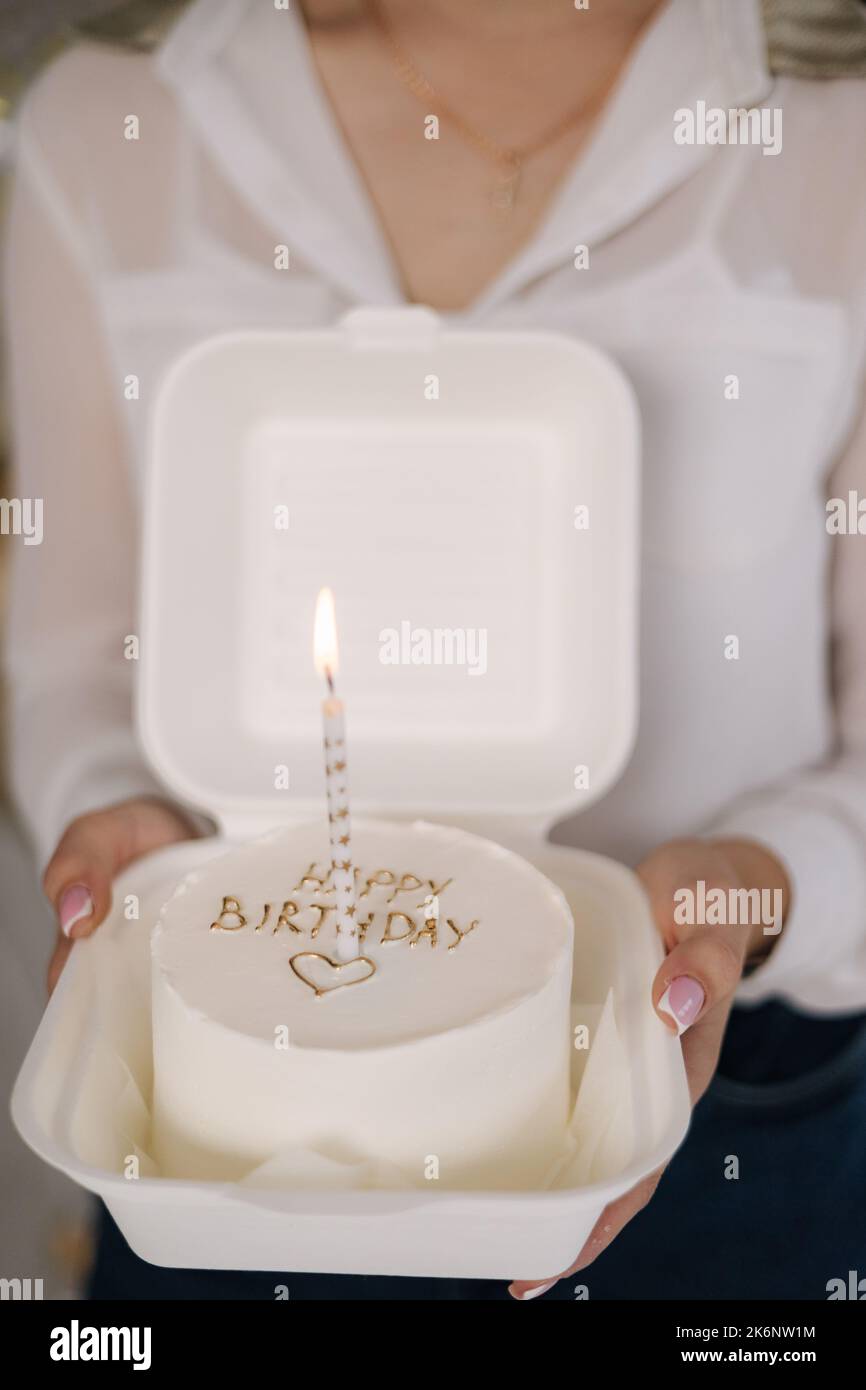 Girl hold bento cake decorated by golden inscription Happy Birthday. Cakes for one person. One candle in the middle of the cake Stock Photo