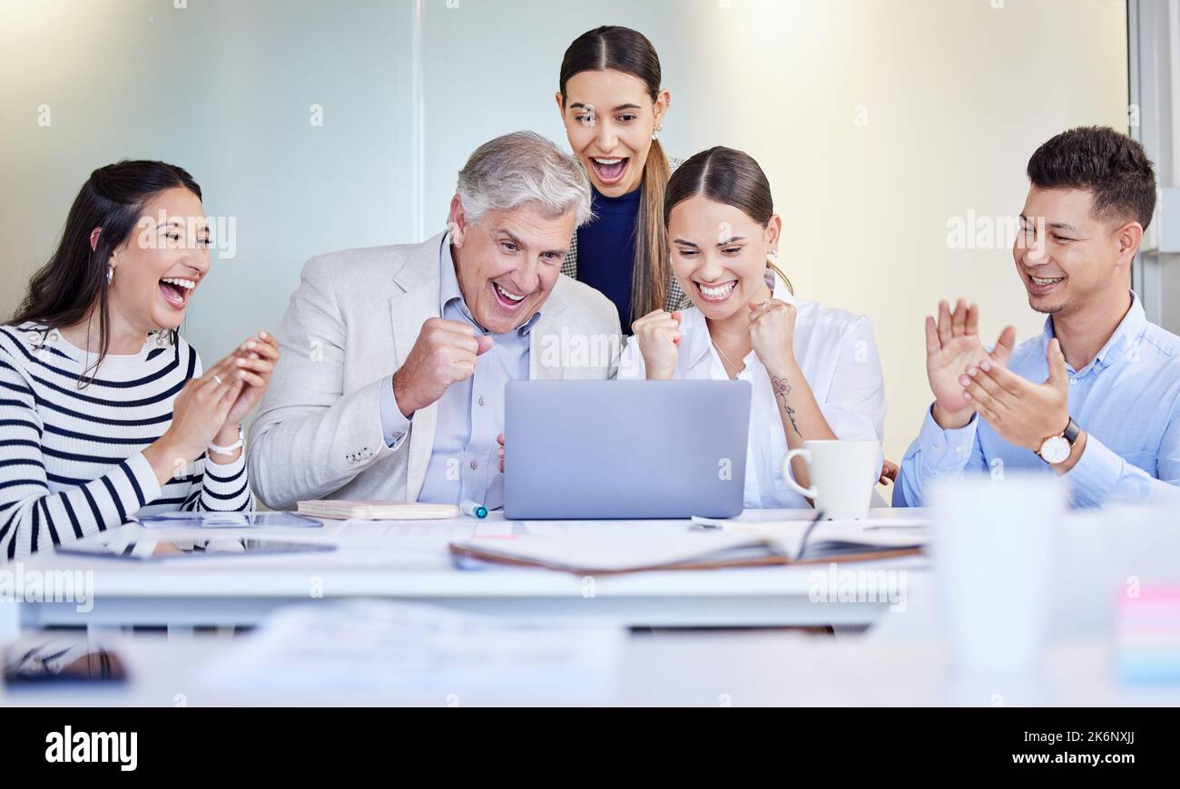 Were on the winning team. a group of businesspeople cheering while using a laptop at work. Stock Photo