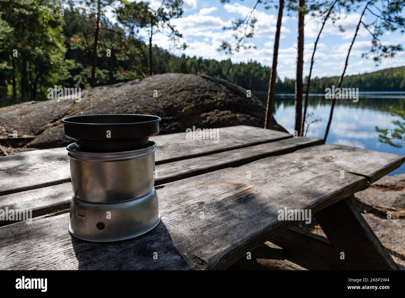 Alcohol-burning, portable stove with a lid on on the wooden table in nature with lake view in the background Stock Photo