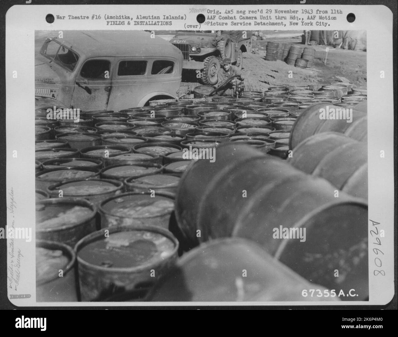 Drums of gasoline are stacked side by side at a fuel dump on Amchitka, Aleutian Islands. Note the truck being refueled. 10 October 1943. Stock Photo