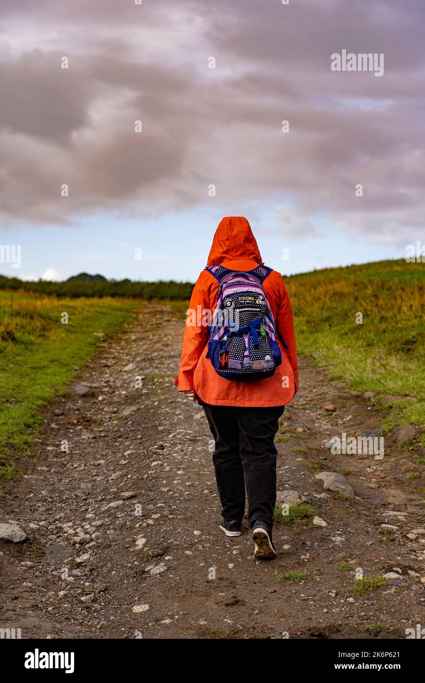 girl in orange coat with back pack walking along a track north yorkshire, UK Stock Photo