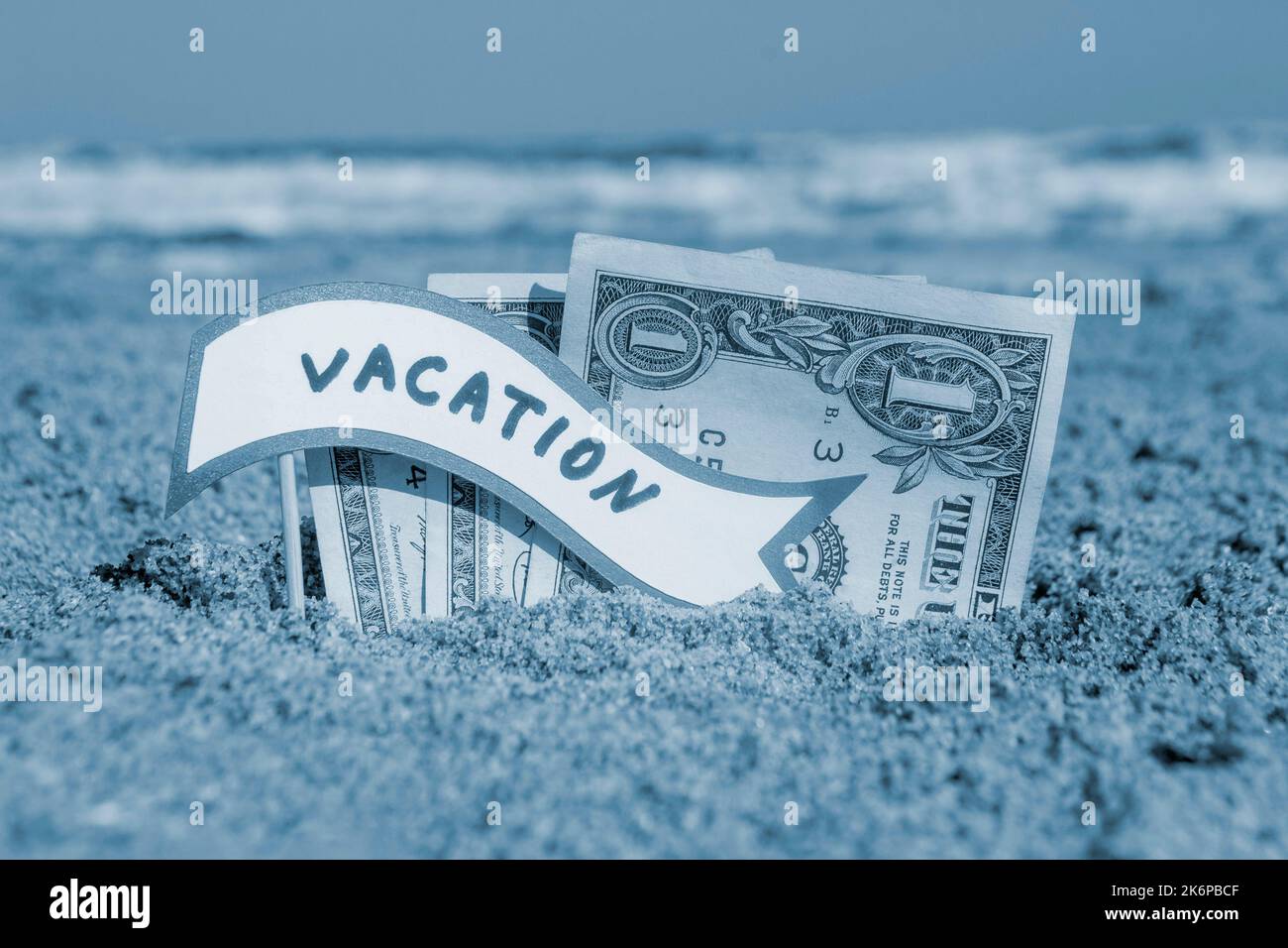 Paper bills one dollar and small stick with paper speech bubble with word Vacation buried in sand beach background sea close-up sunny summer day. Concept Money travel tourism vacation Blue white color Stock Photo