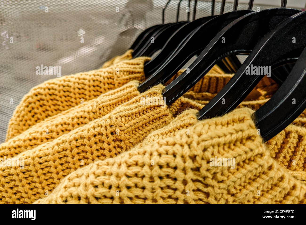 Yellow sweaters hanging on clothing rack for sale in fast fashion, mass