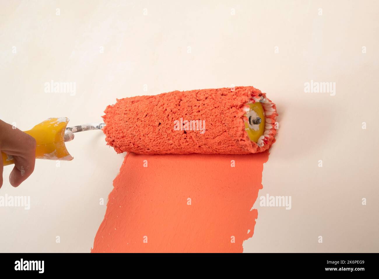 painting the wall orange color, paint roller. Stock Photo