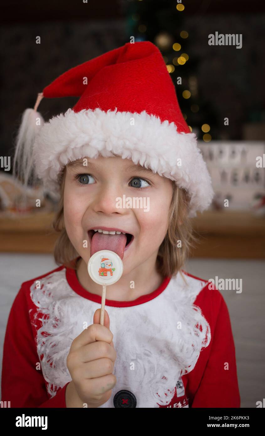 cute boy in red santa hat licks sweet holiday lollipop. sweet holiday