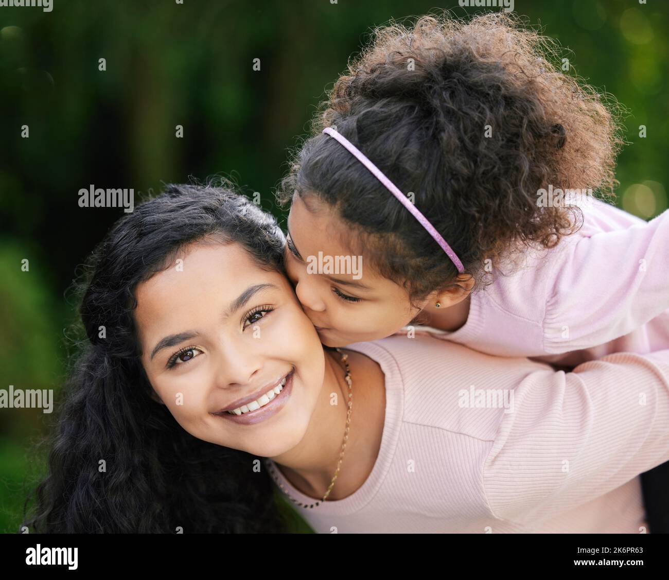 Happiness is seeing your kids happy. a little girl giving her mother a kiss on the cheek outdoors. Stock Photo