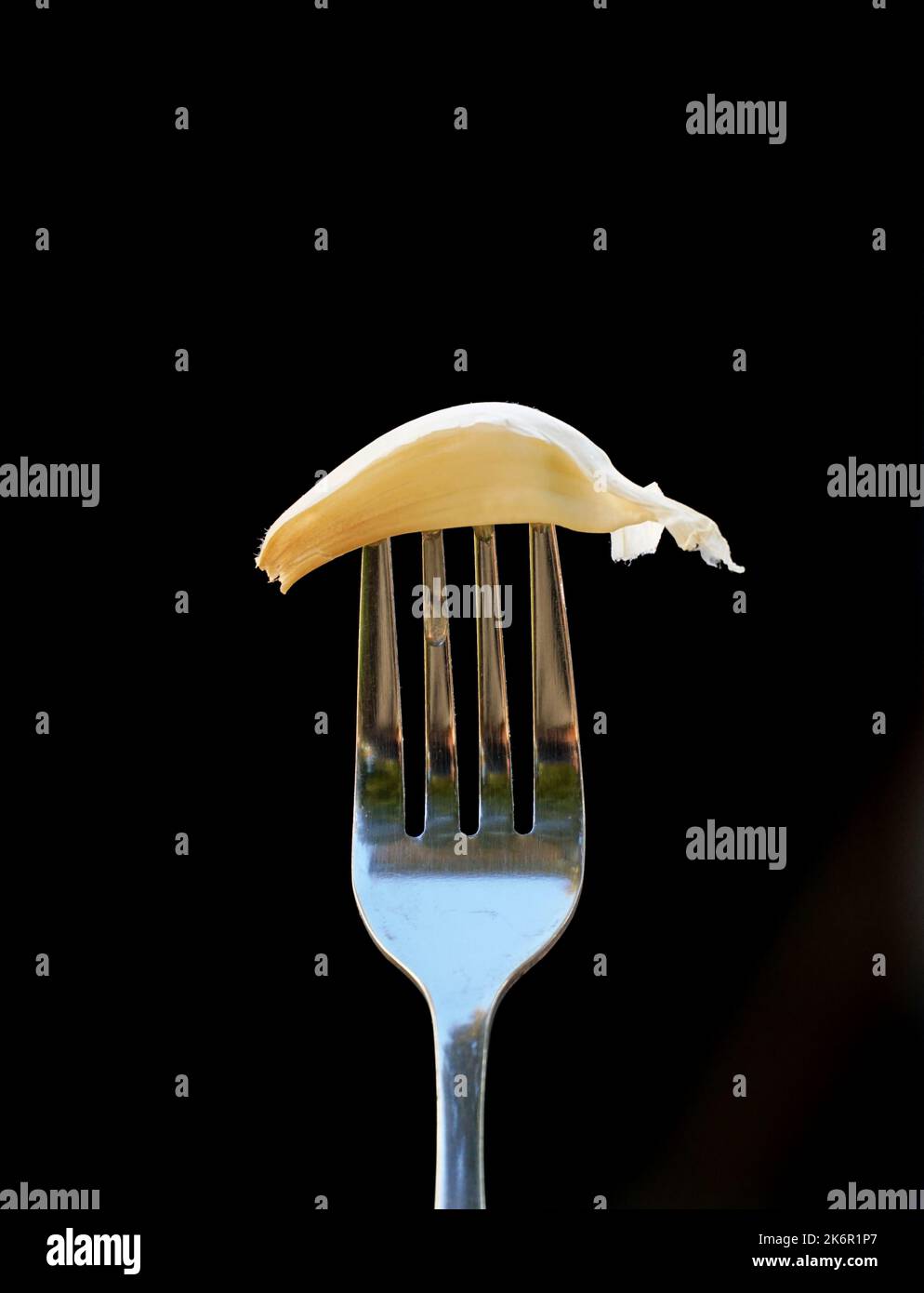single garlic clove on fork on black background Stock Photo - Alamy