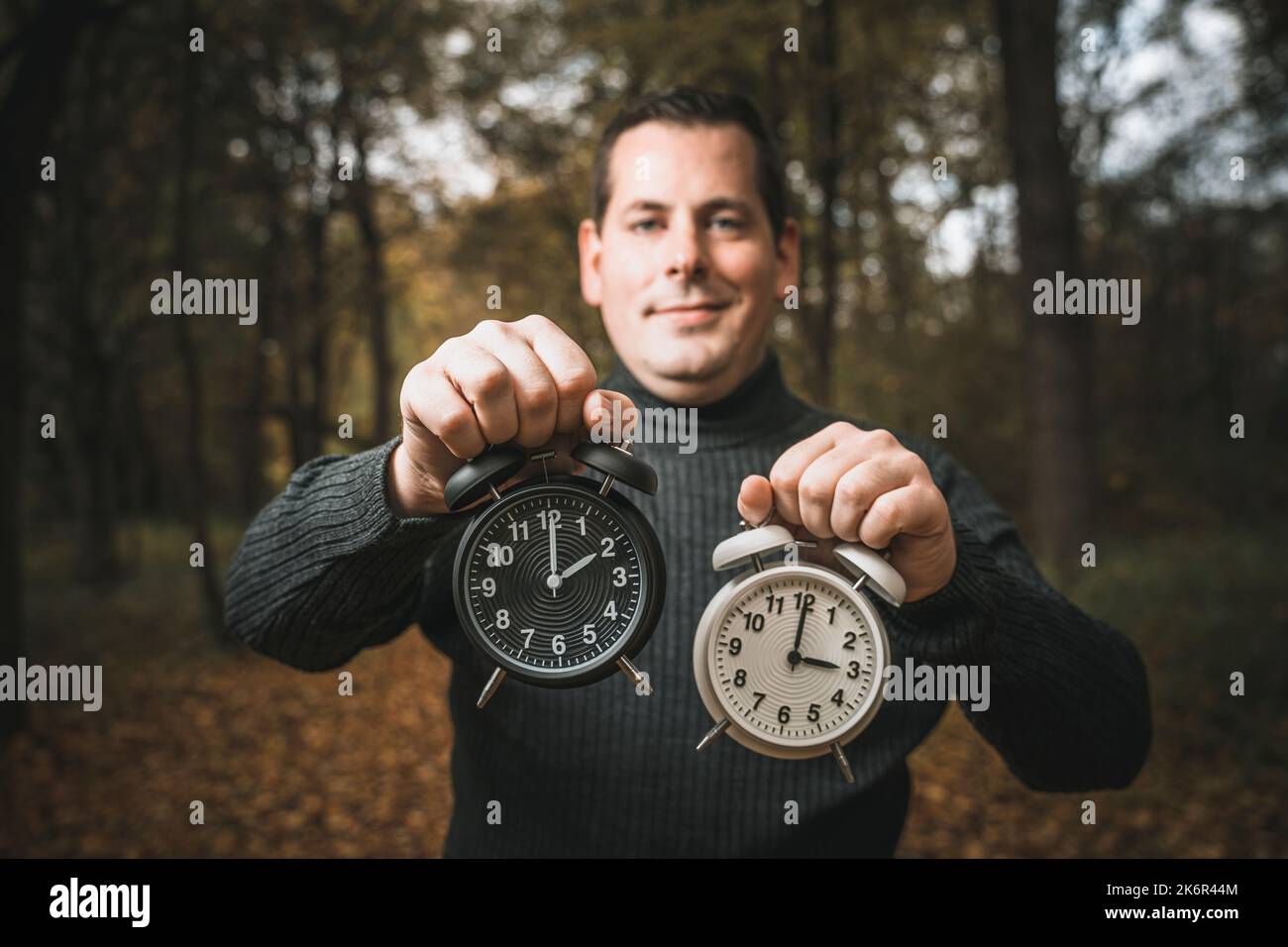 14 October 2022 A Man Holding Two Alarm Clocks In The Forest, Daylight