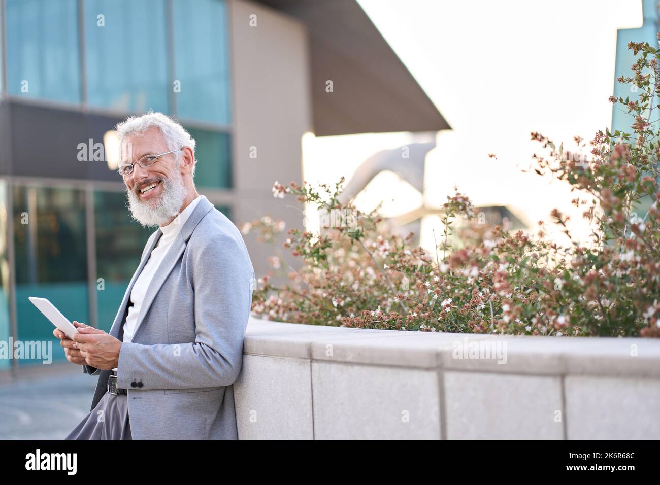 Smiling older business man using digital tablet standing outside city buildings. Stock Photo
