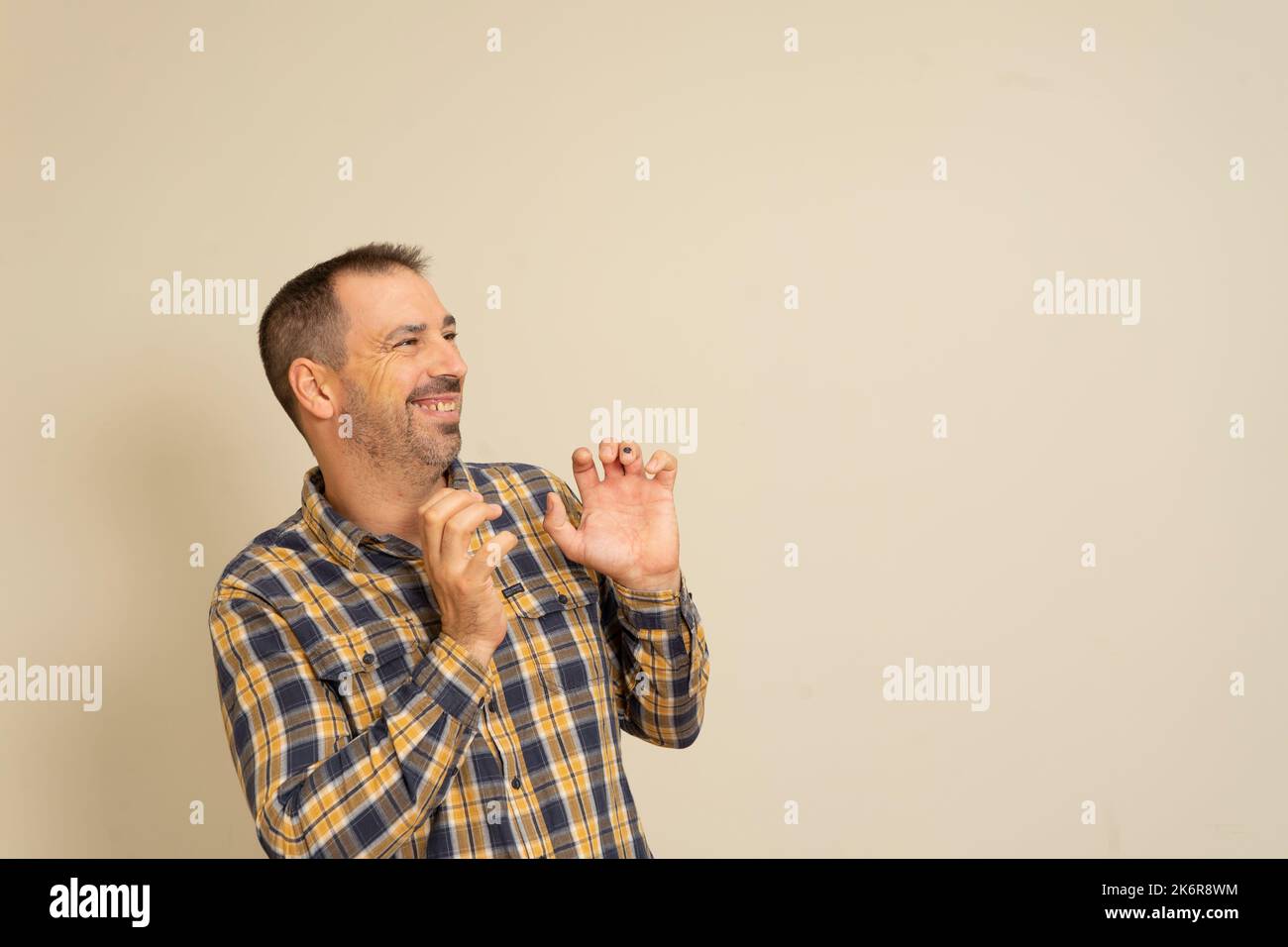 Hispanic man with a beard nervously playing with his hands. Shame. Isolated beige background. Negative emotions facial expression feeling Stock Photo