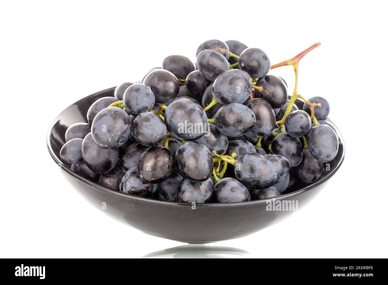 One sprig of sweet black grapes in a ceramic plate, macro, isolated on white background. Stock Photo