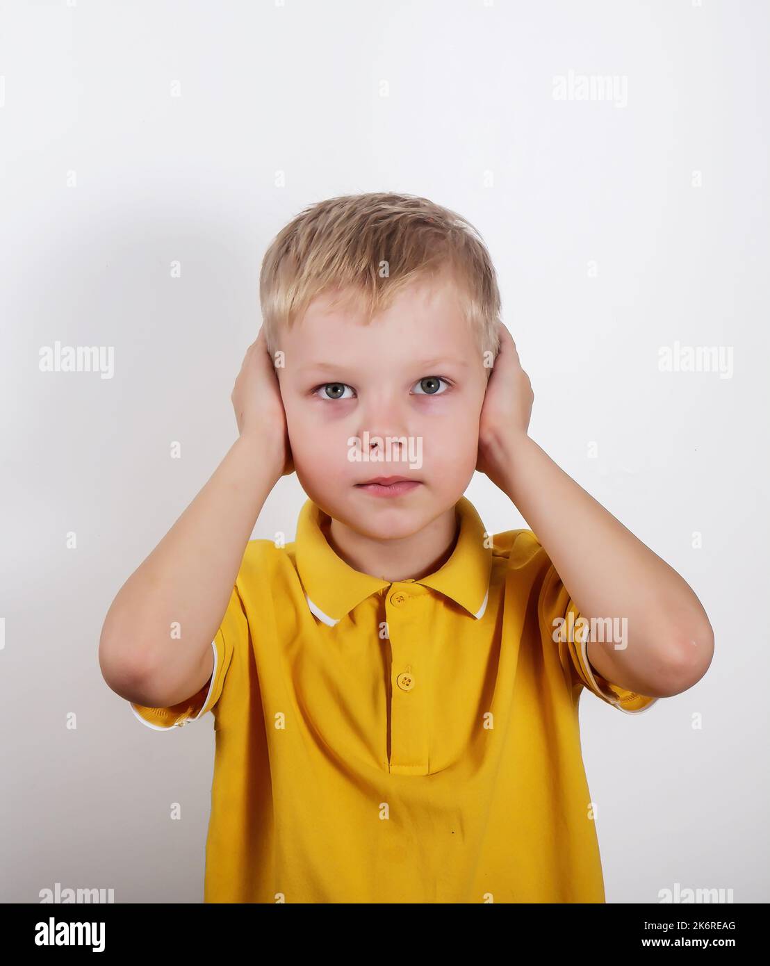 a boy in a yellow Tshirt shows covering his ears with both hands, isolated on a white