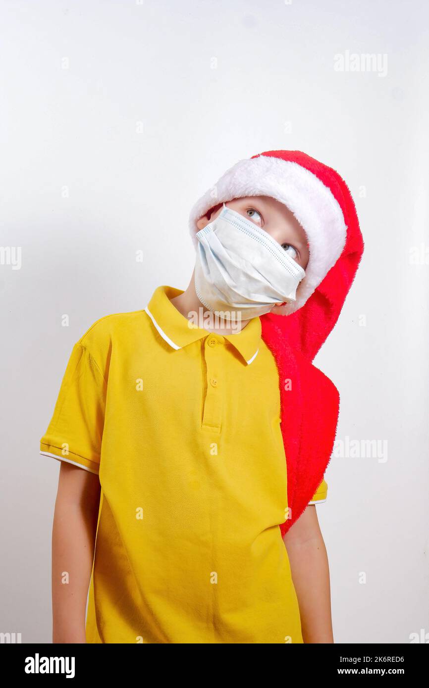 a boy in a yellow T - shirt .Santa Claus's New Year's hat and medical mask looks away, isolated on a white background. Stock Photo