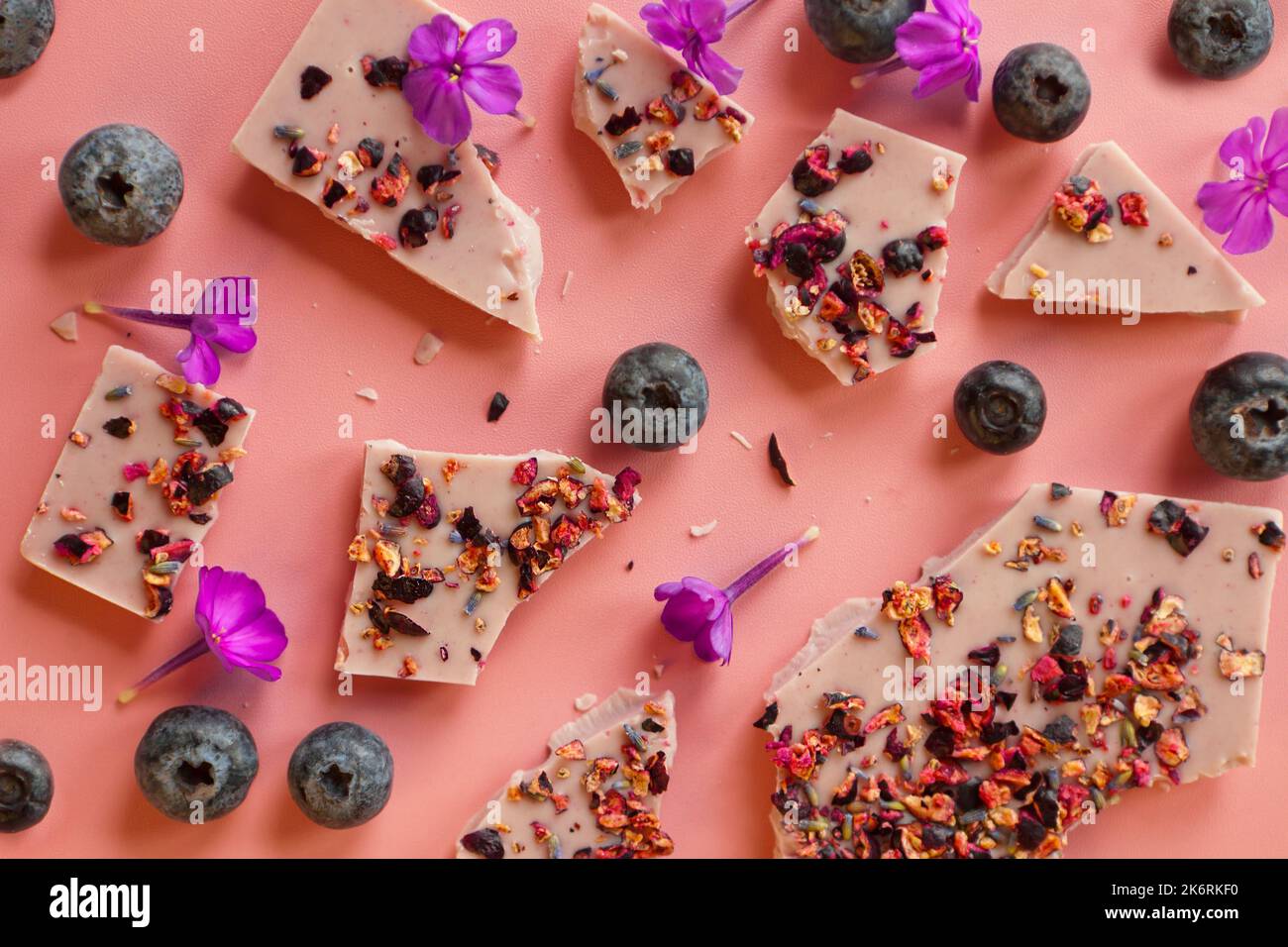 crushed pink chocolate with blueberries and flowers. Broken bars with nuts and sublimated raspberry Stock Photo