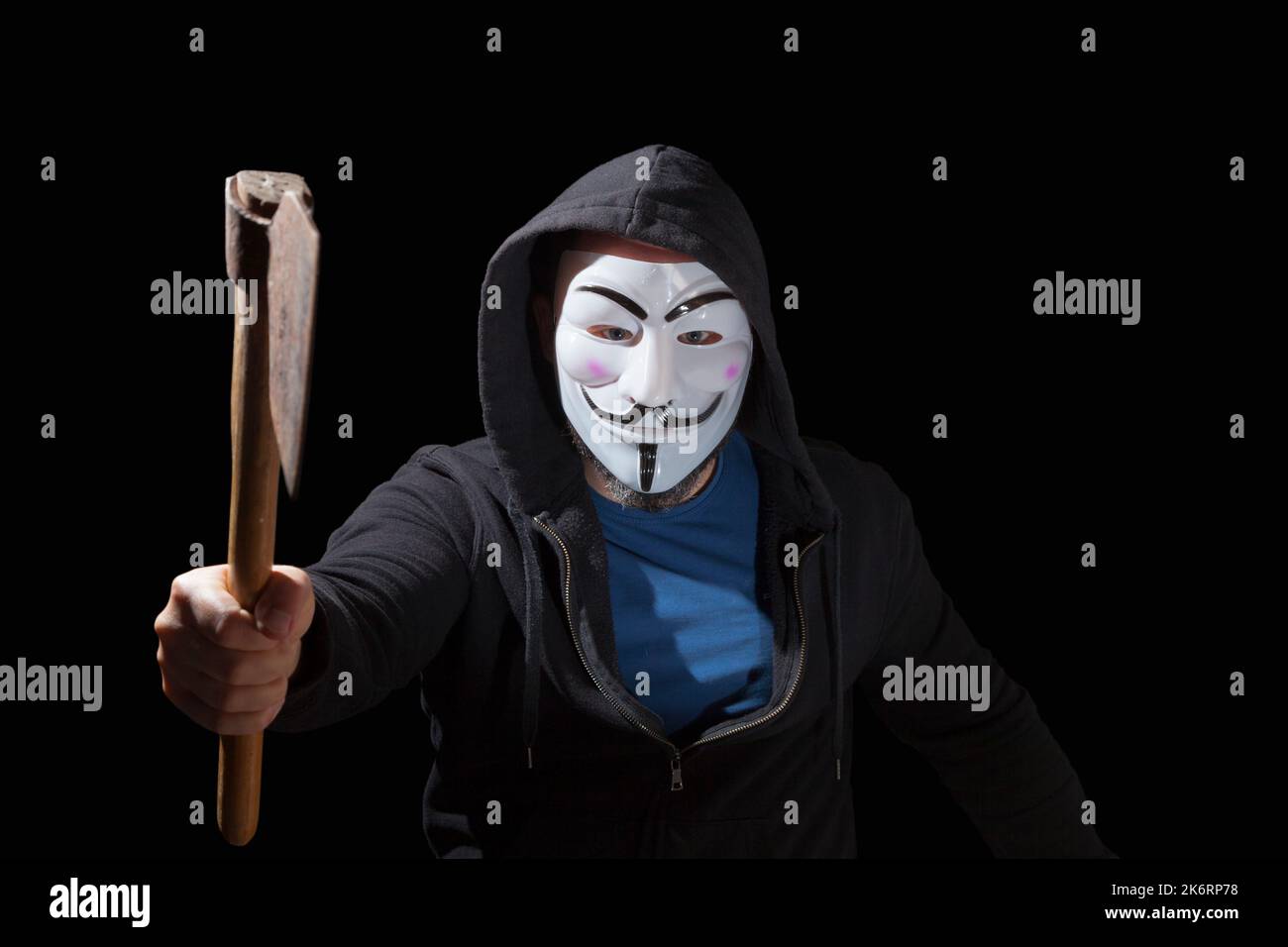 Man wearing a mask and a hoodie brandishing a armed a hatchet on black background. Stock Photo
