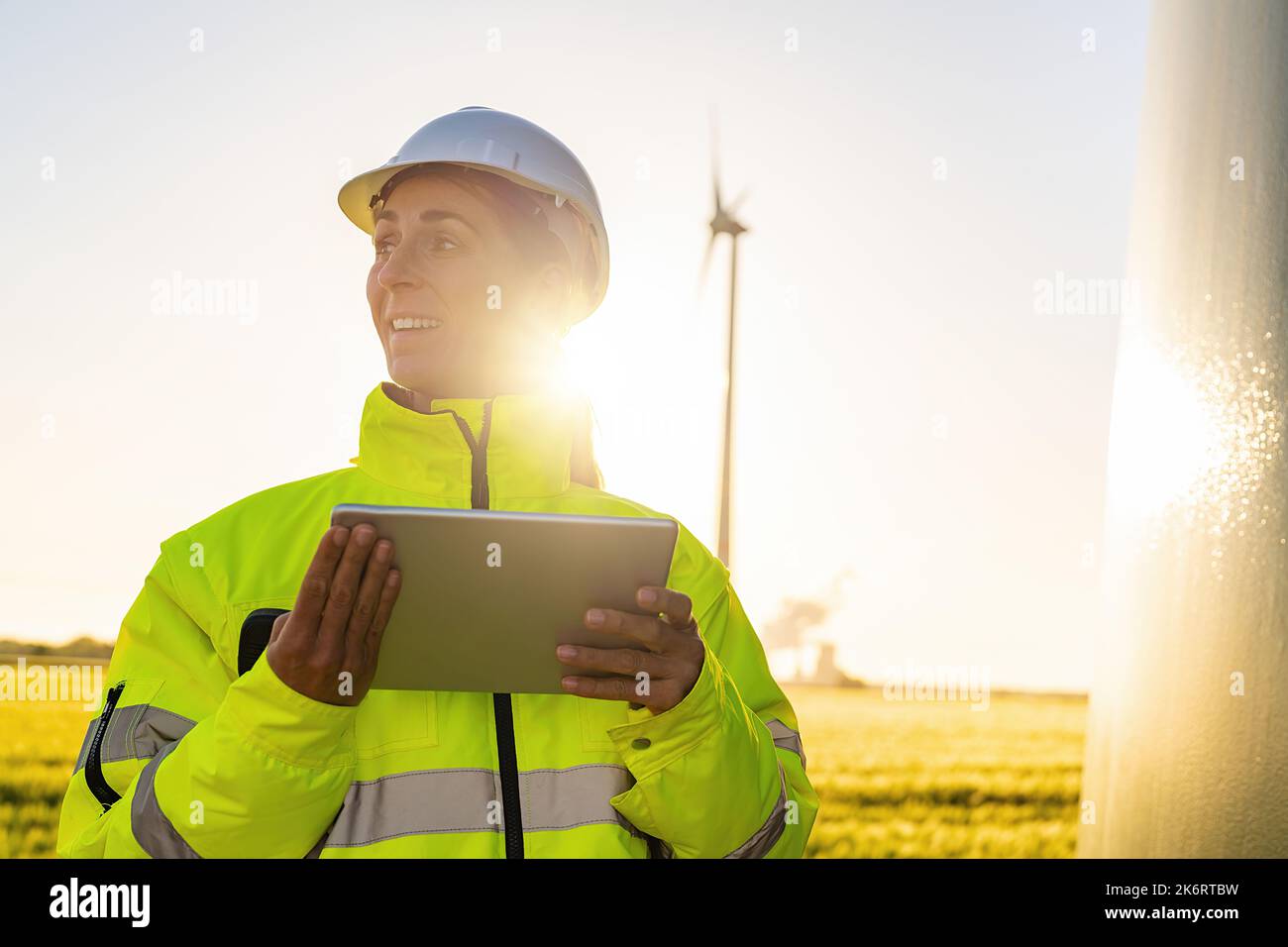 Young female engineer holding tablet looking and checking wind turbines at field Stock Photo