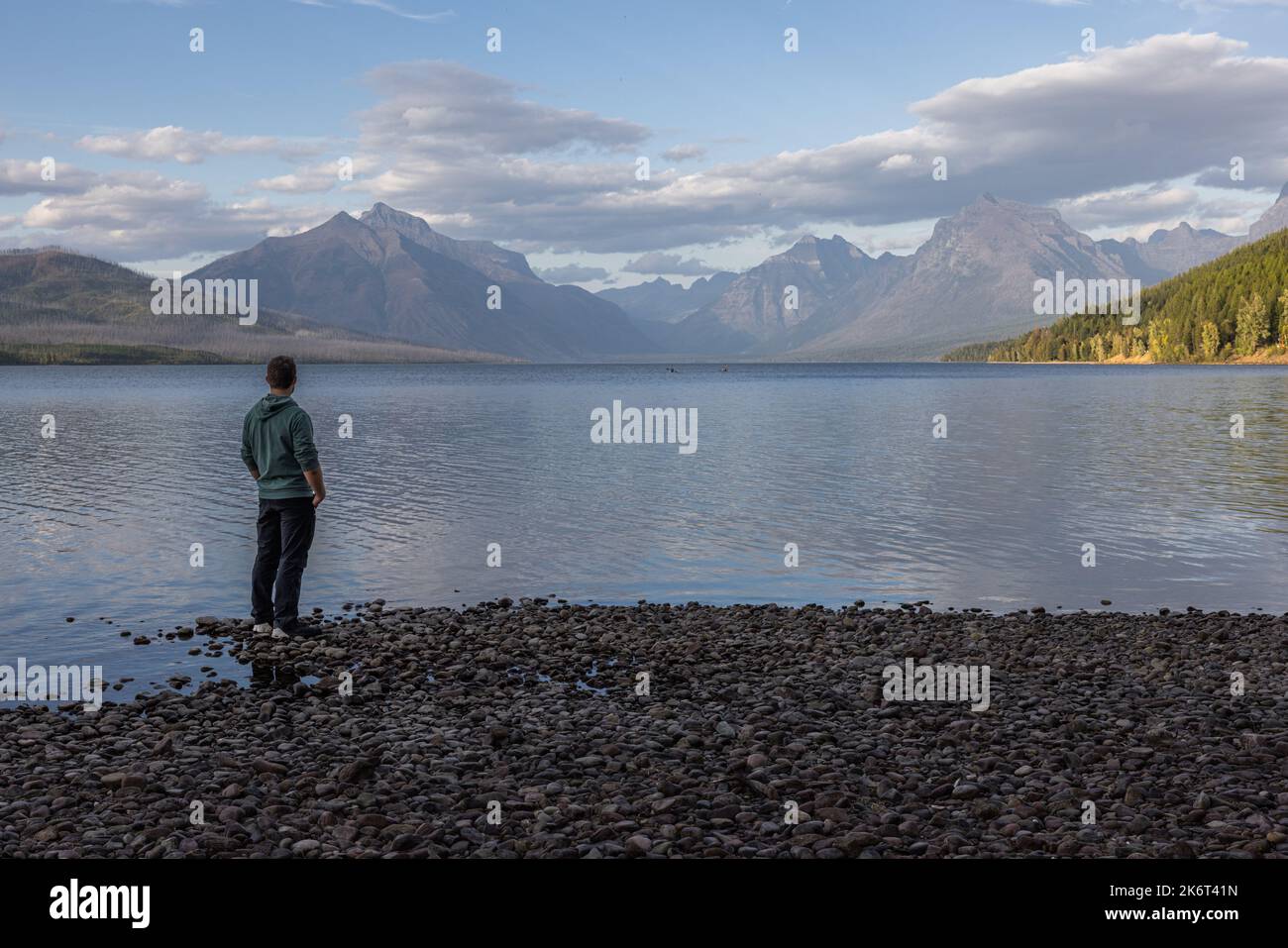 Man standing on the shoreline looking at the amazing mountains across lake McDonald in Glacier National Park Stock Photo