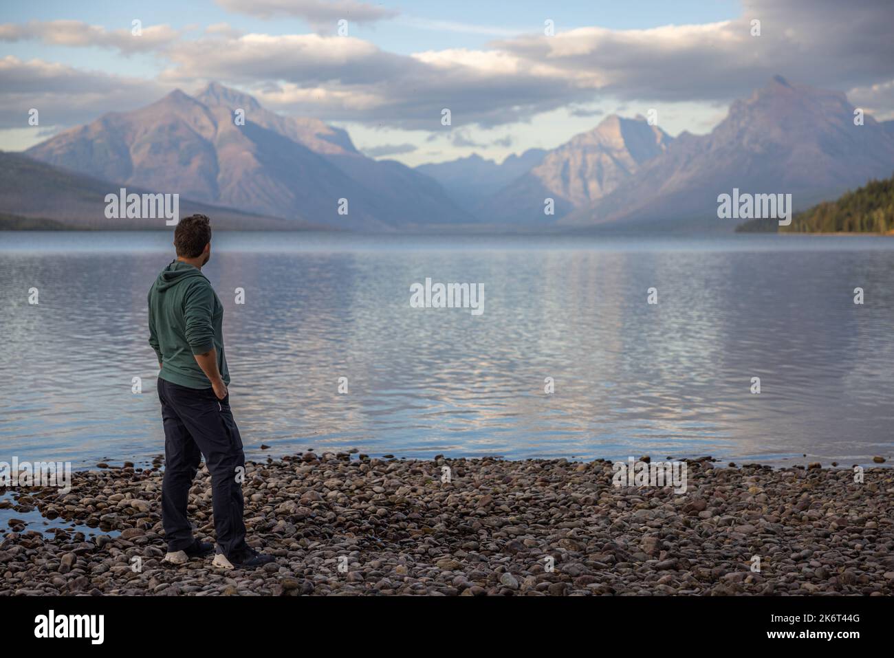 Man standing on the shoreline looking at the amazing mountains across lake McDonald in Glacier National Park Stock Photo